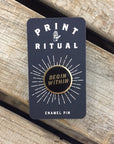 Black circle enamel pin with "begin within" in gold with gold border on print ritual card backing