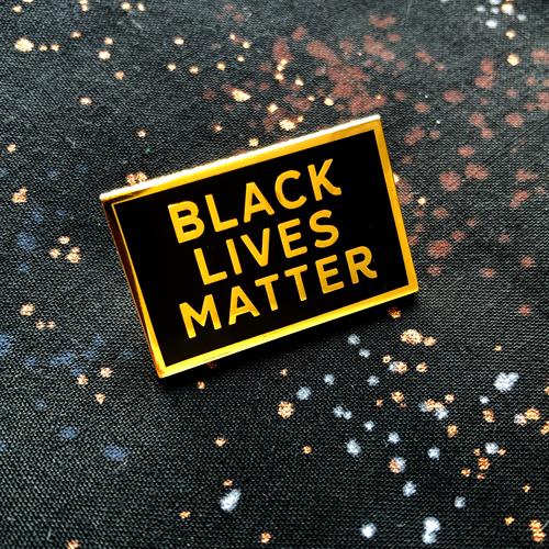 "Black Lives Matter" in gold block text on black enamel pin
